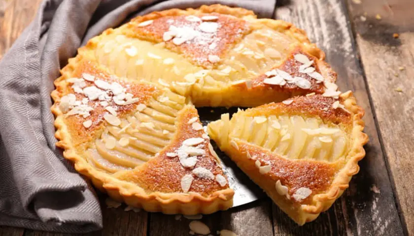 Une délicieuse tarte au poire, garnie d'amandes effilées et saupoudrée de sucre glace, repose sur un plateau en bois.