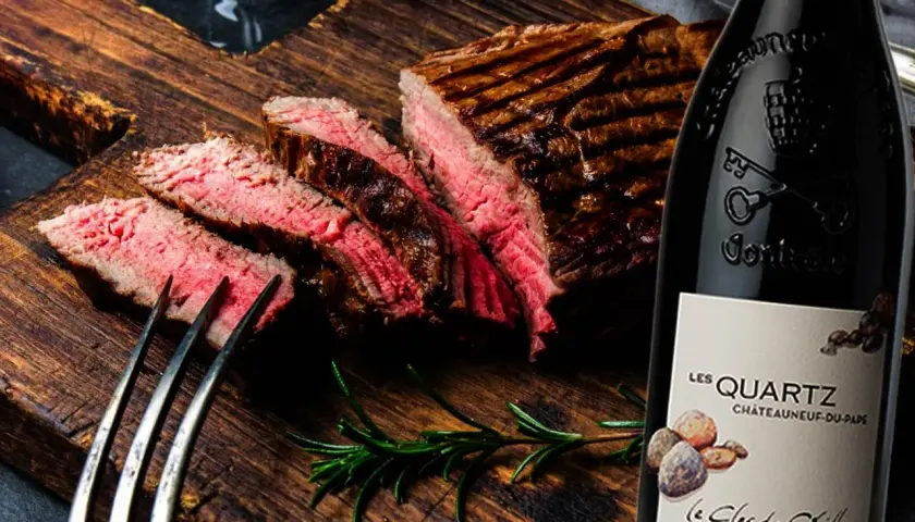 Un steak grillé et tranché sur une planche en bois, accompagné d'une bouteille de vin rouge passe partout.