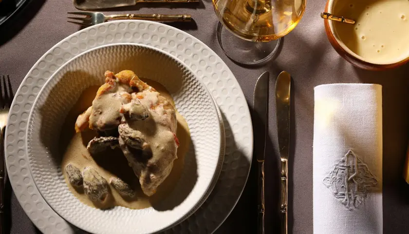 Un plat de poulet au vin jaune, crémeux et garni de morilles, servi sur une assiette texturée. Une table dressée avec élégance.