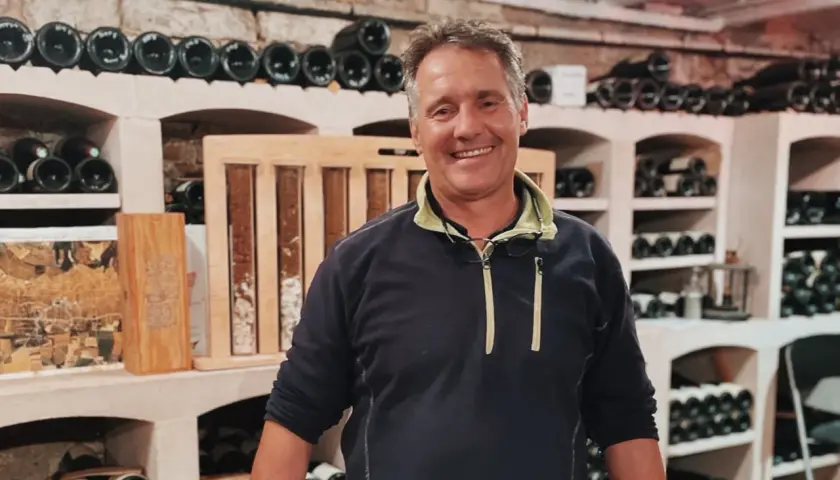 Bruno Clavelier, vigneron souriant, pose dans sa cave remplie de bouteilles.