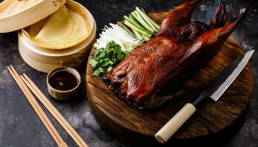 Un canard laqué prêt à être dégusté, accompagné de ses crêpes, sauce, légumes croquants et coriandre. Une recette parfaite pour un repas festif.