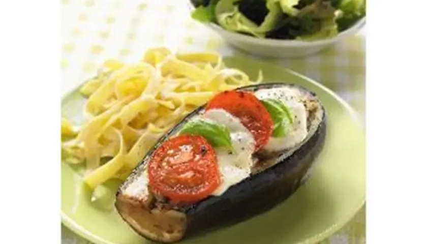 Aubergine farcie de mozzarella, tomates et basilic, servie avec des pâtes et une salade verte. Un plat savoureux et coloré.