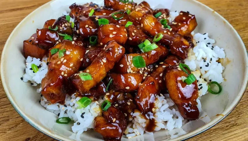 Un plat appétissant de porc au caramel asiatique, garni de graines de sésame et d'oignons verts, servi sur du riz blanc. Une recette à essayer !