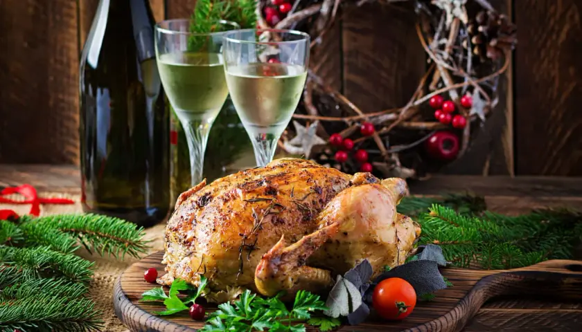 Un chapon rôti, prêt à être dégusté, avec deux verres de vin blanc et une décoration festive. Quel vin avec du chapon pour ce repas de fête ?