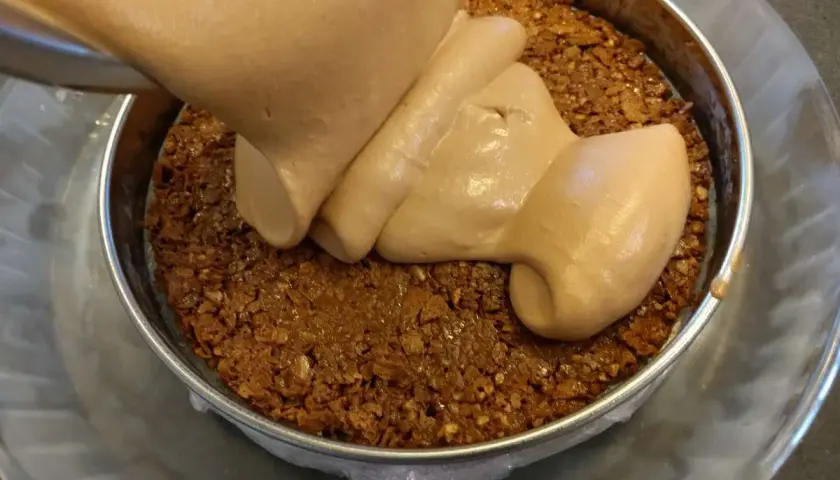 Une crème onctueuse est versée sur une base croustillante praliné feuilletine dans un cercle à pâtisserie.