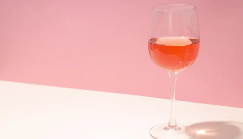 Un verre de rosé de macération, d'une belle couleur orangée, sur un fond rose et blanc.
