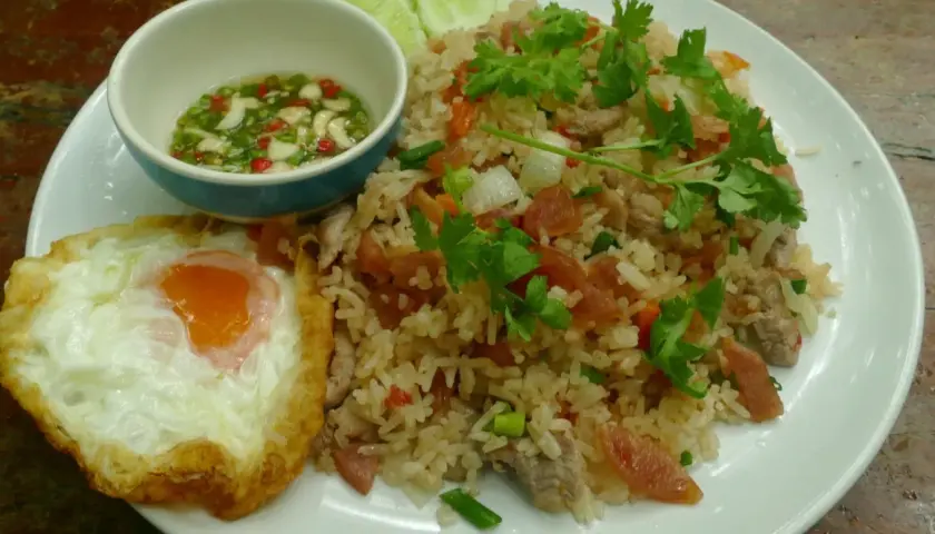 Un plat de riz thaï savoureux avec un œuf au plat, des tranches de concombre et une sauce piquante.