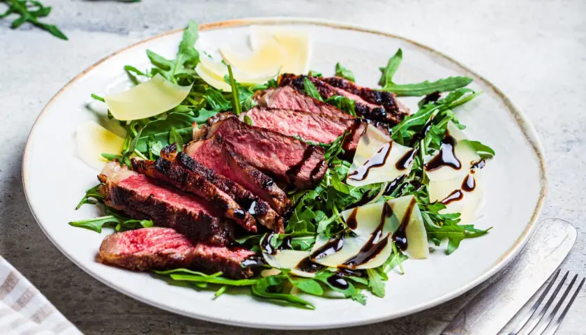 Une assiette de tagliata de boeuf, roquette, copeaux de parmesan et filet de vinaigre balsamique.