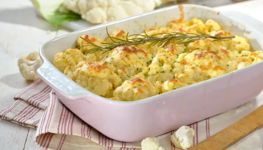 Un plat de gratin de chou-fleur doré et gratiné, garni de romarin frais, prêt à être dégusté.