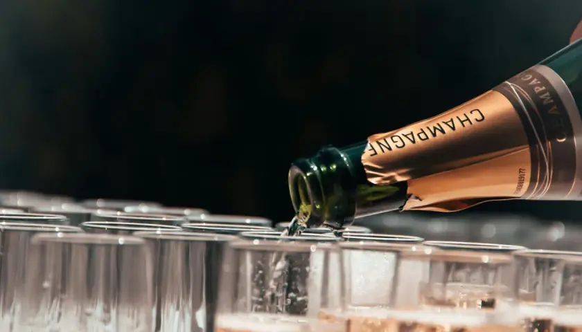 Une bouteille de champagne verse dans des flûtes alignées. Le choix idéal pour quel champagne choisir pour l'apéritif.