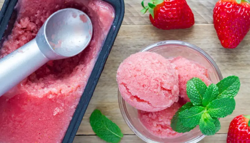 Un délicieux parfait glacé à la fraise, servi dans un bol avec des feuilles de menthe fraîche et des fraises entières.
