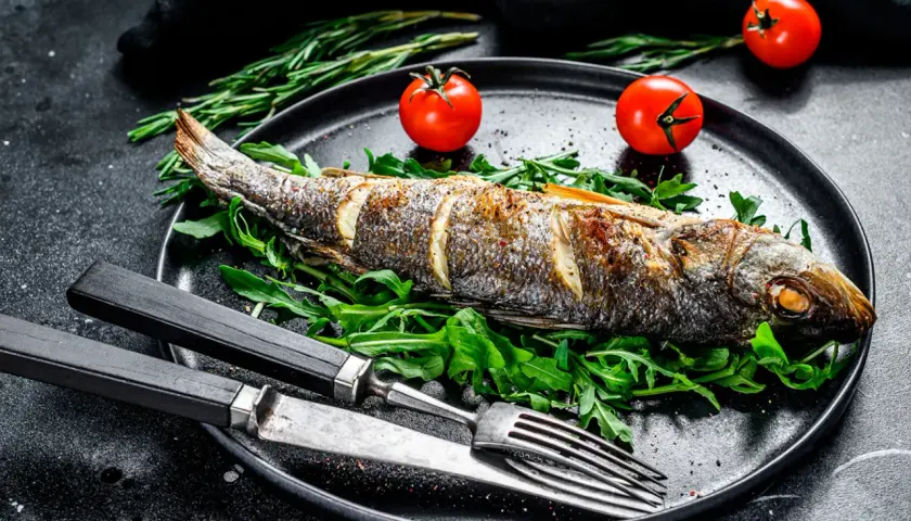 Bar au barbecue, entier et doré, servi sur un lit de roquette avec des tomates cerises et des herbes. Un délice à savourer !