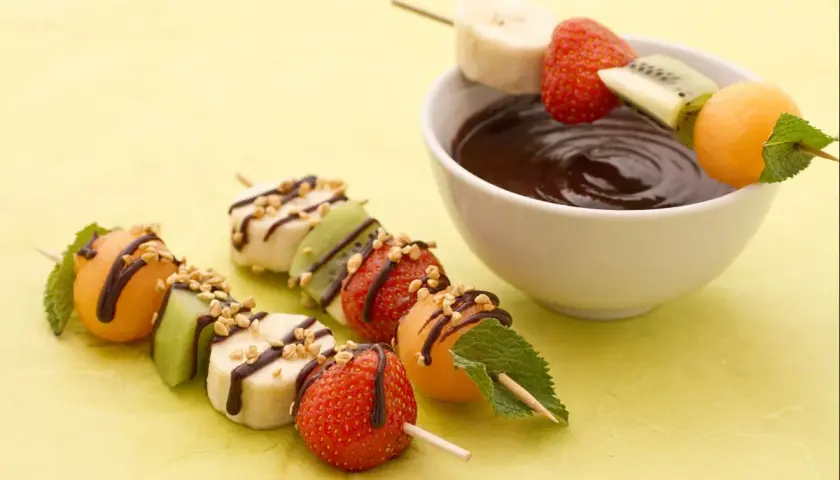 Délicieuses brochettes de fruits, bananes, fraises, kiwis et melons, arrosées de chocolat et de noix, prêtes à être trempées.