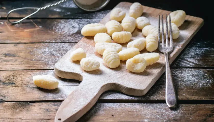 Gnocchis faits maison, prêts pour la cuisson. Une fourchette et une passoire à farine sur une planche en bois saupoudrée de farine, parfaits pour une recette de gnocchi.