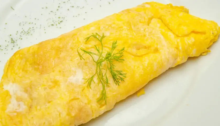 Une omelette au thon, dorée et moelleuse, garnie d'aneth frais sur une assiette blanche. Un délice simple et savoureux.