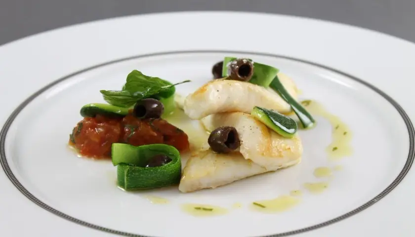Délicieux filet de saint pierre poêlé, servi avec une concassée de tomates, des rubans de courgette et des olives noires.