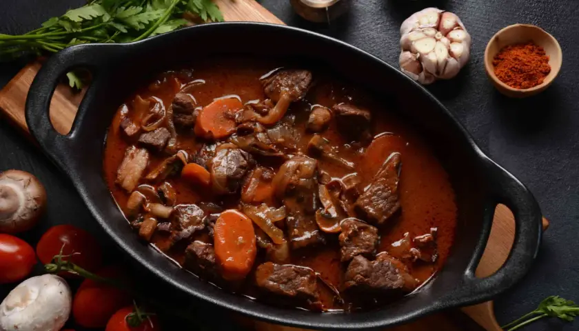Un plat mijoté de bœuf bourguignon traditionnel, avec des carottes, des oignons et des champignons, prêt à être dégusté.