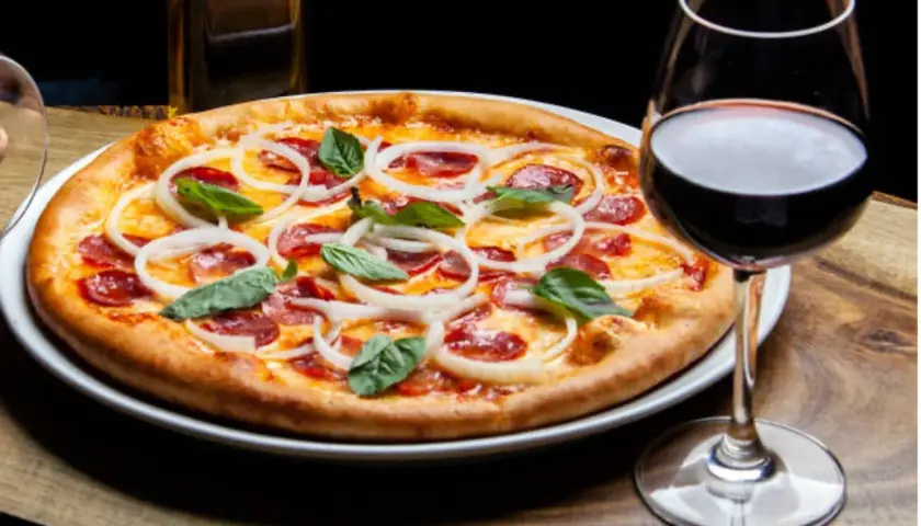 Une pizza garnie d'oignons et de pepperoni, accompagnée d'un verre de vin rouge. La question est : quel vin avec pizza ?