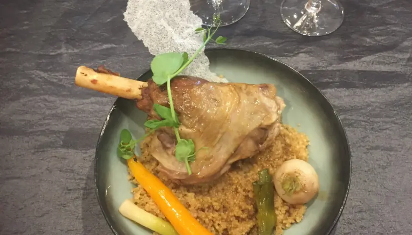 Souris d'agneau braisée au vin, servie sur un lit de couscous avec carottes et navets. Un plat savoureux et réconfortant.