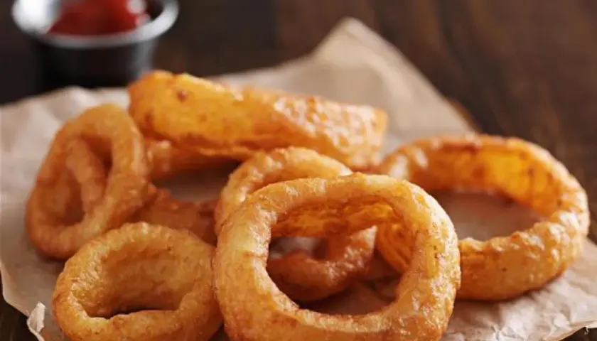Un tas d'oignon rings dorés et croustillants, servis sur du papier brun, avec un petit bol de ketchup en arrière-plan.