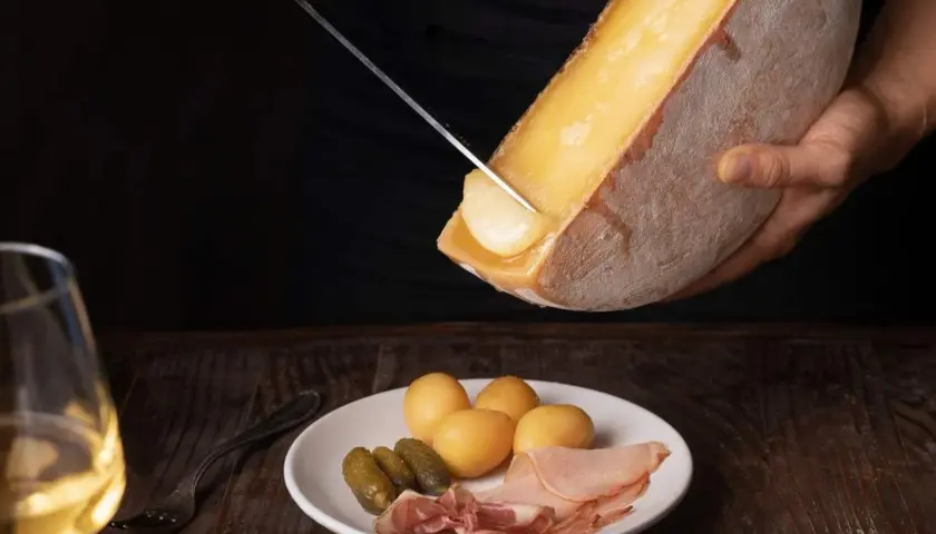 Un verre de vin blanc, parfait pour accompagner la raclette. Sur l'assiette, pommes de terre, cornichons et charcuterie.