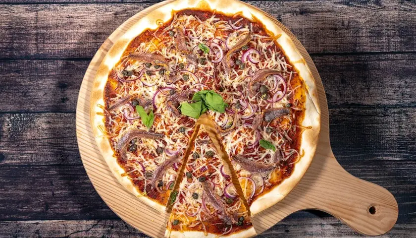 Une pizza savoureuse aux anchois, oignons rouges et câpres, garnie de fromage râpé et de basilic frais, prête à être dégustée.