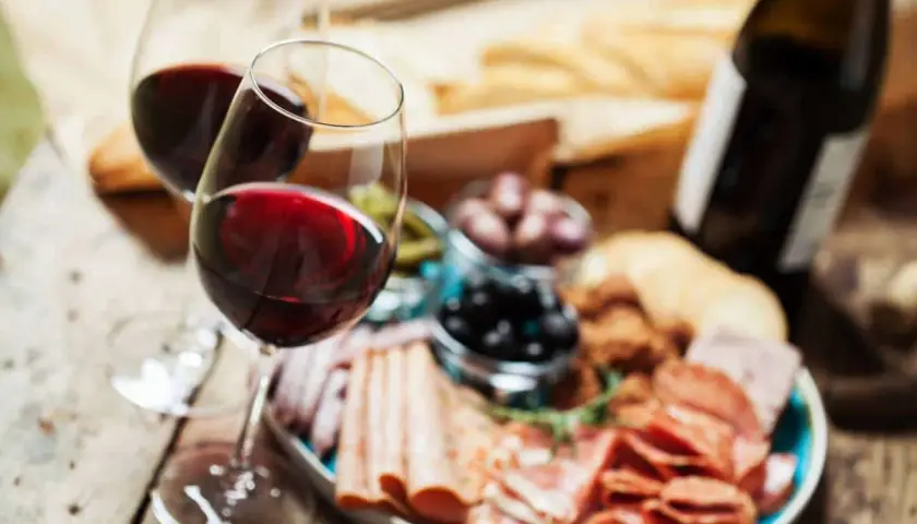 Deux verres de vin rouge, une bouteille, une assiette de charcuterie variée, olives et cornichons. Parfait pour savoir quel vin avec charcuterie.
