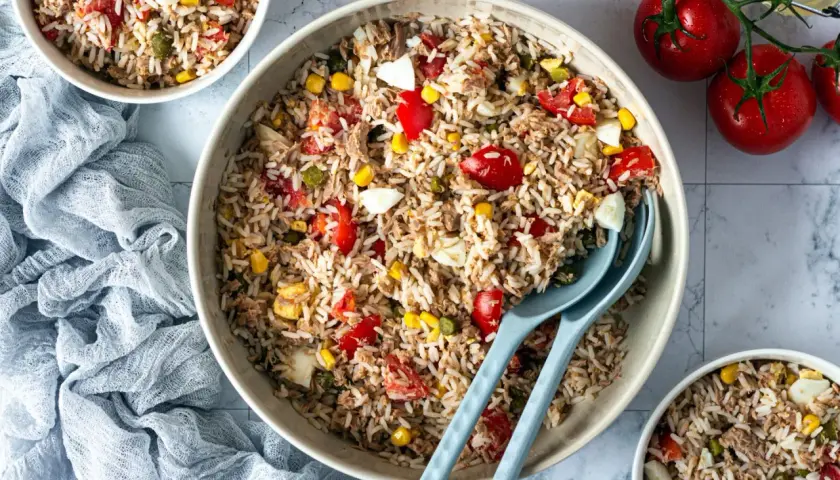 Un grand bol de salade de riz thon, garnie de tomates, maïs et œufs durs. Parfait pour un repas léger et savoureux.