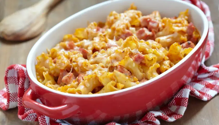 Un plat de gratin de pâtes au jambon, doré et gratiné, servi dans un plat rouge sur une serviette à carreaux.