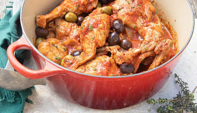 Un plat mijoté de lapin aux olives, baignant dans une sauce tomate savoureuse, garni de thym frais.