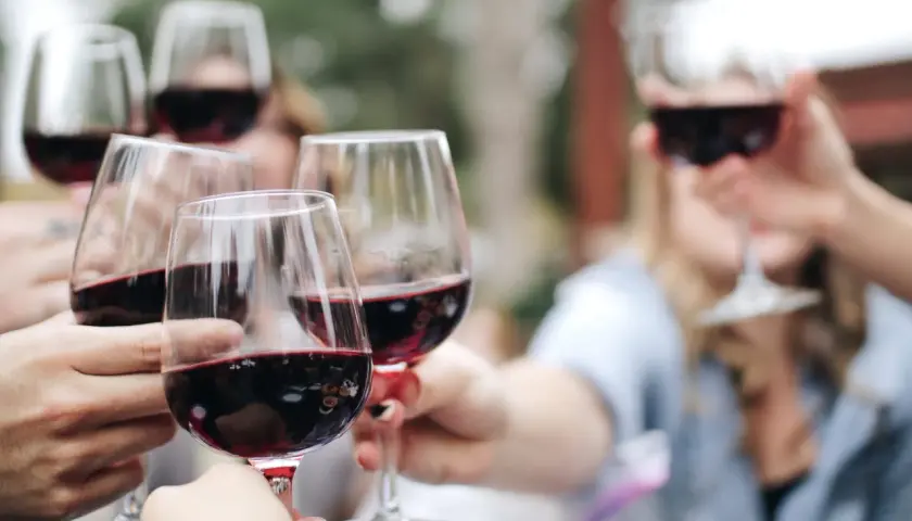 Des mains portent des verres remplis de vin rouge pour une dégustation conviviale en plein air.