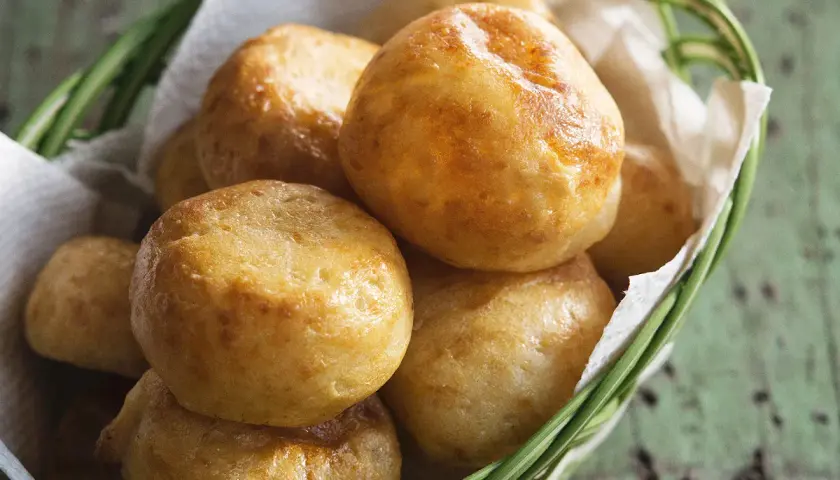 Petits pains dorés, une délicieuse recette de manioc, servis dans un panier en osier garni de papier blanc.