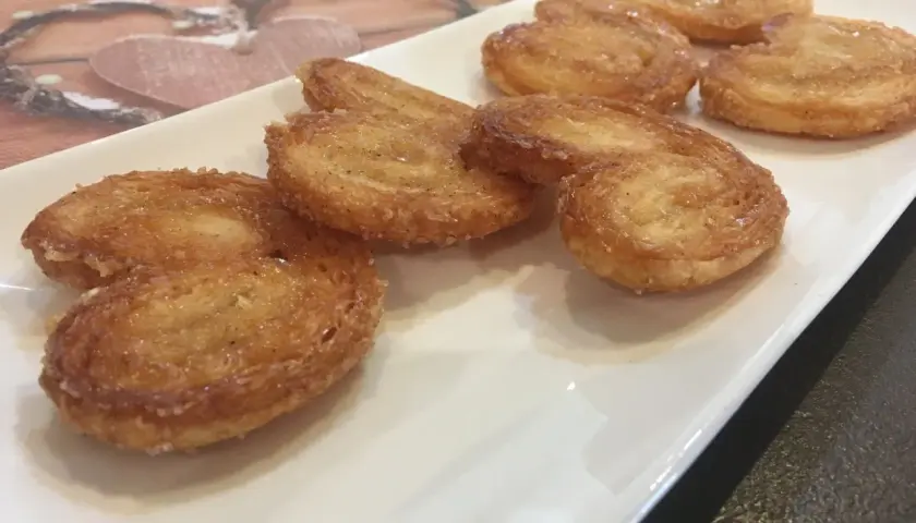 Une assiette blanche présente plusieurs palmiers croustillants, parfaits pour une recette facile.