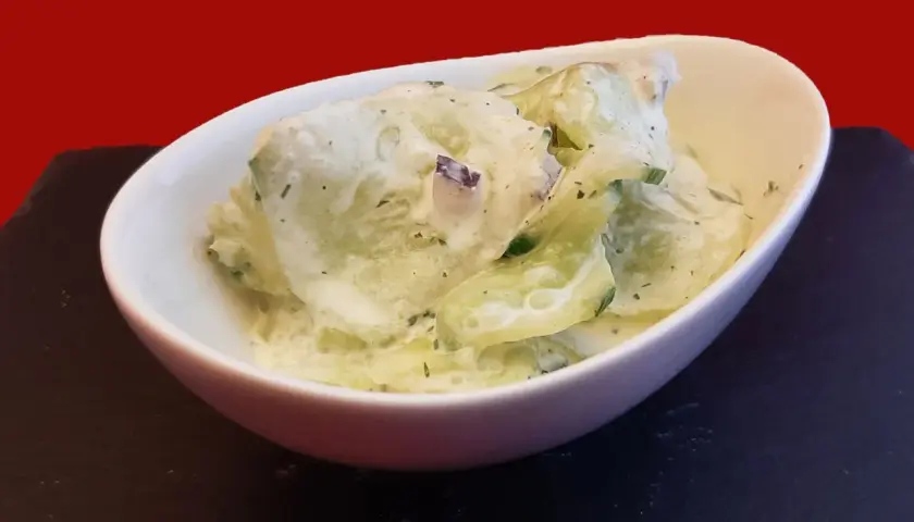 Un bol de concombre à la crème, garni d'herbes fraîches, prêt à être dégusté.