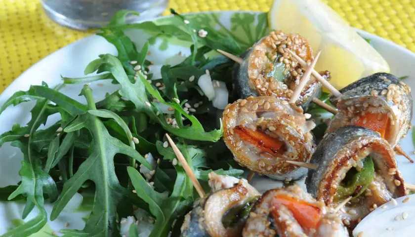 Rouleaux de sardines à la plancha, enrobés de sésame, servis avec une salade verte et un quartier de citron.