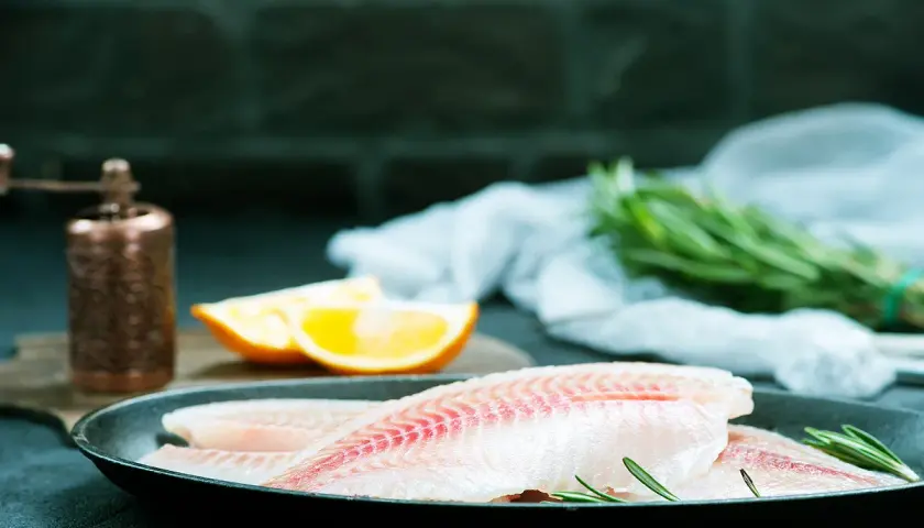 Filets de poisson crus dans une poêle, prêts pour un maquereau au vin blanc. Oranges et romarin à proximité.