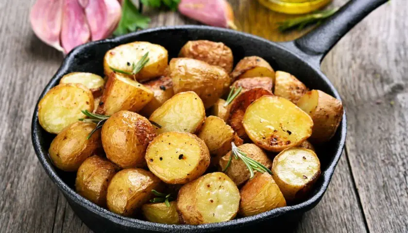 Poêlée de pommes de terre sautées dorées et croustillantes, garnies de romarin frais, avec de l'ail et de l'huile d'olive en arrière-plan.