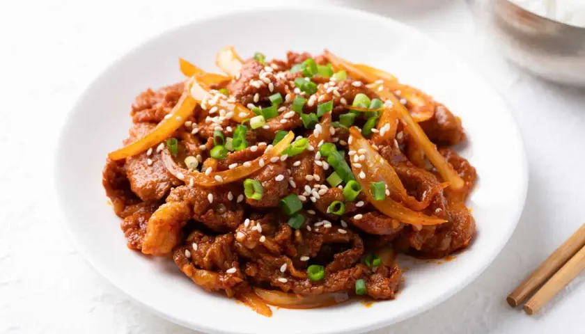 Délicieux boeuf aux oignons, garni de graines de sésame et de ciboule, servi sur une assiette blanche.