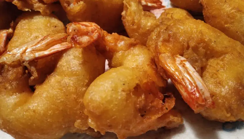 Gros plan sur des beignets de crevette dorés et croustillants, prêts à être dégustés. Les queues des crevettes dépassent de la pâte.