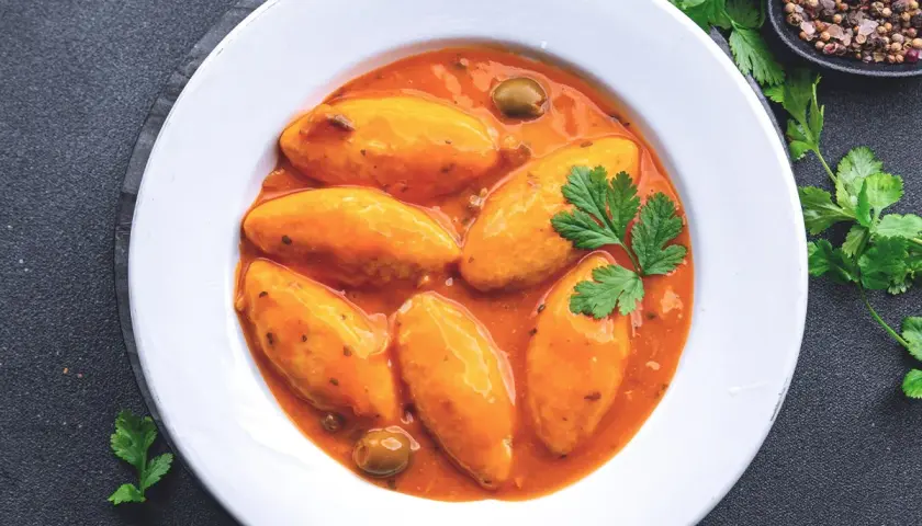Assiette de quenelles de brochet en sauce tomate, garnie de persil et d'olives.