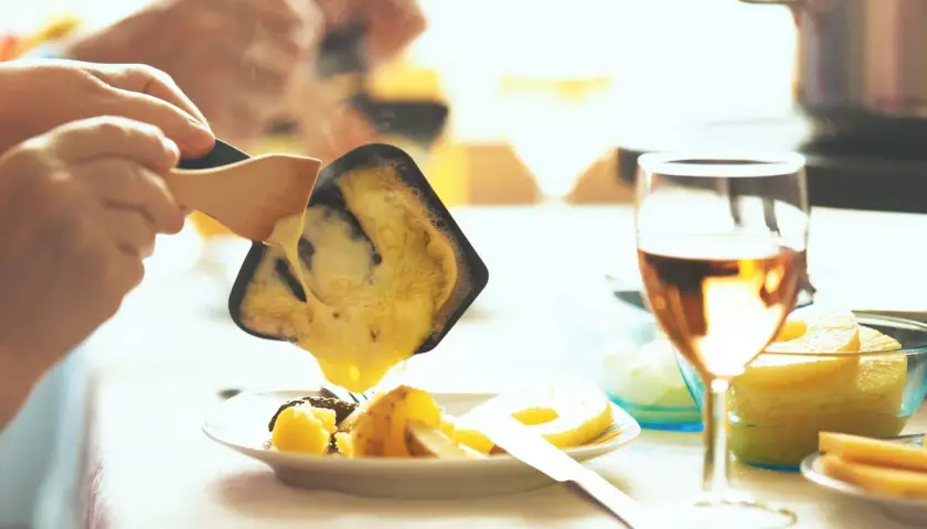 Raclette fondue dégoulinant sur des pommes de terre, un verre de Bourgogne Aligoté à côté.