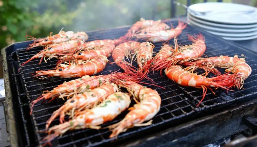 Grosses gambas barbecue sur un grill, fumant et appétissant. Les crevettes sont bien caramélisées, prêtes à être dégustées.