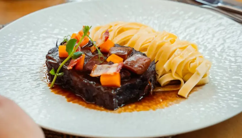 Un paleron de bœuf braisé, garni de dés de carottes et de lardons, servi avec des tagliatelles fraîches. Une recette savoureuse à découvrir.