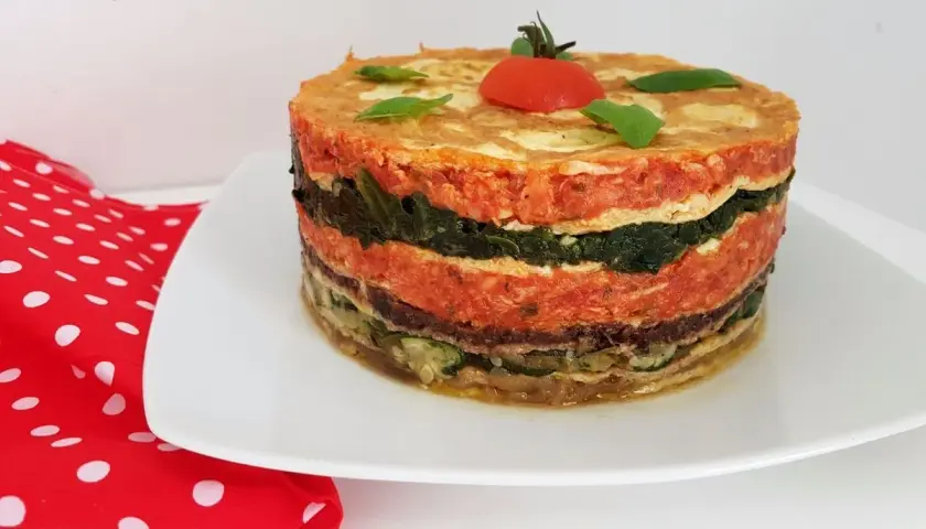 Un délicieux gâteau d'omelette provençale, aux couches colorées de légumes et de sauce tomate, garni d'une tomate cerise.