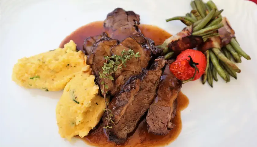 Savoureux sabodet au vin rouge, servi avec une polenta crémeuse, des haricots verts enroulés de lard et une tomate confite.