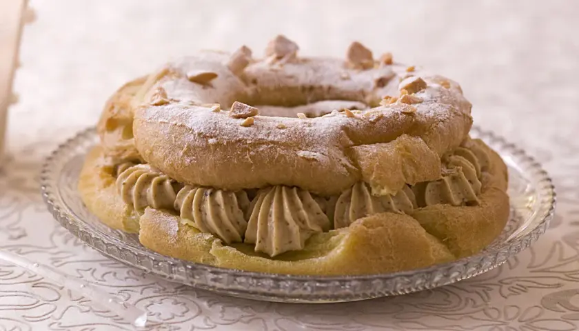 Un Paris-Brest garni d'une généreuse crème mousseline praliné, saupoudré de sucre glace et d'éclats de noisettes.