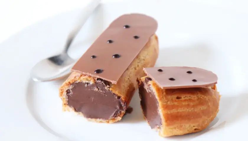 Deux éclairs au chocolat, un entier et un coupé, sur une assiette blanche avec une cuillère. Parfait pour une recette éclair au chocolat.
