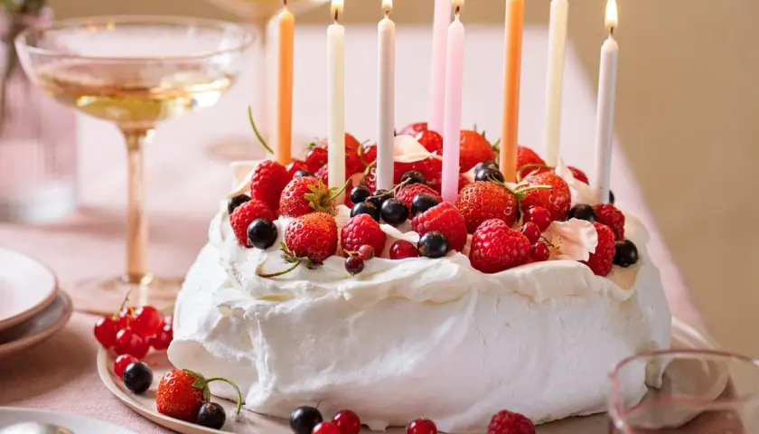 Pavlova fruit rouge, ornée de fraises, framboises et myrtilles, avec des bougies allumées pour une fête gourmande.