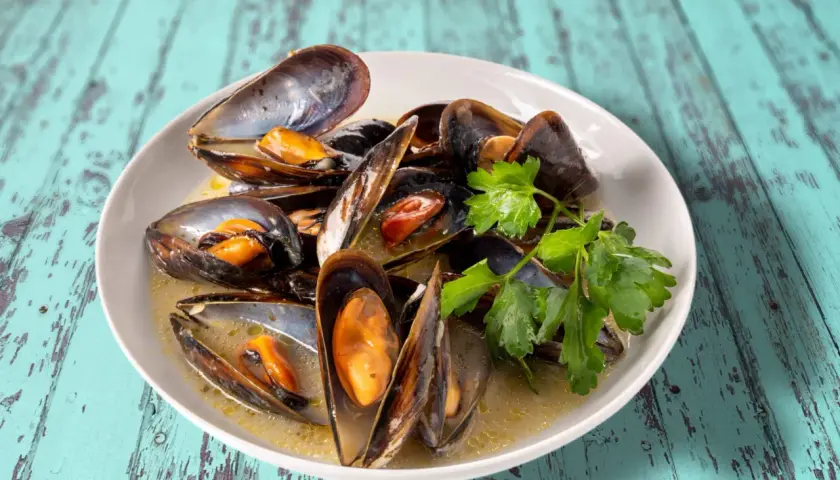 Un plat de moules au roquefort, garni de persil frais, baignant dans une sauce crémeuse. Un délice savoureux sur une table en bois bleu délavé.