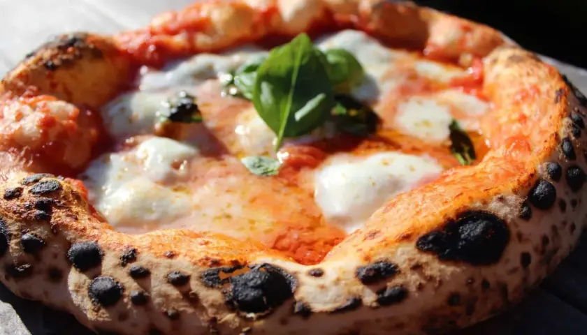 Une pizza napolitaine authentique, avec sa croûte gonflée et tachetée, garnie de sauce tomate, mozzarella fondante et basilic frais. La recette parfaite pour un délice italien.